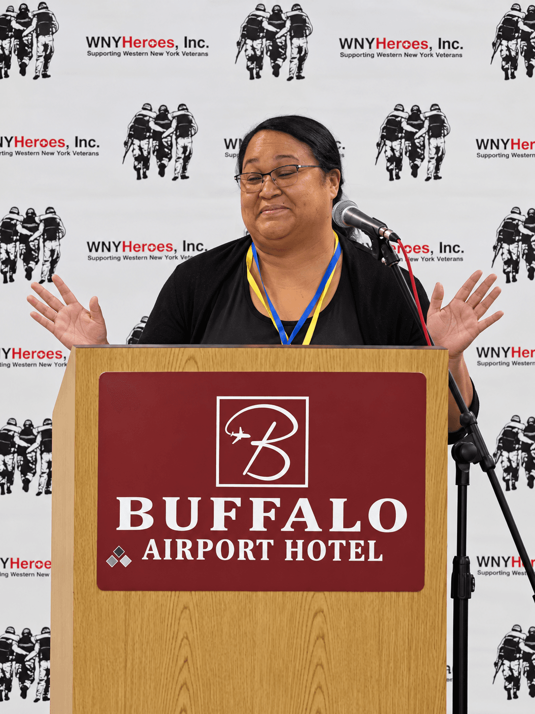 Darlin Brown speaking from a podium at a WNYHeroes event, hands open mid-sentence.